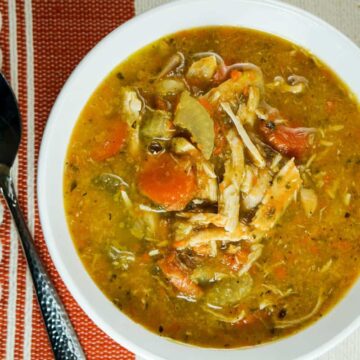 Bowl of chicken vegetables soup on burnt orange and white tablecloth and spoon