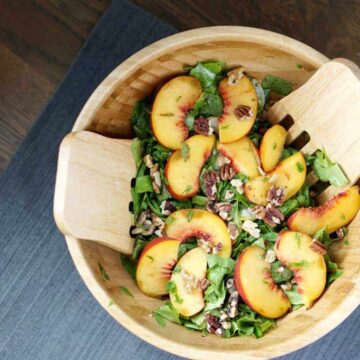 This toasted pecan, cucumber, basil, and peach salad in a large wooden bowl with wooden salad spoons on a darker wooden table is super fresh and incorporates summer and fall flavors into one great gluten and dairy free dish. It's also super quick and sugar-free