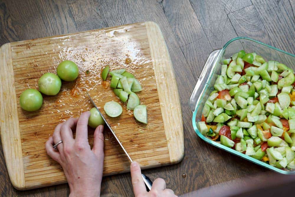 slicing tomatillos and tomatoes for a Mexican casserole on a wooden cutting board on a dark wood table.