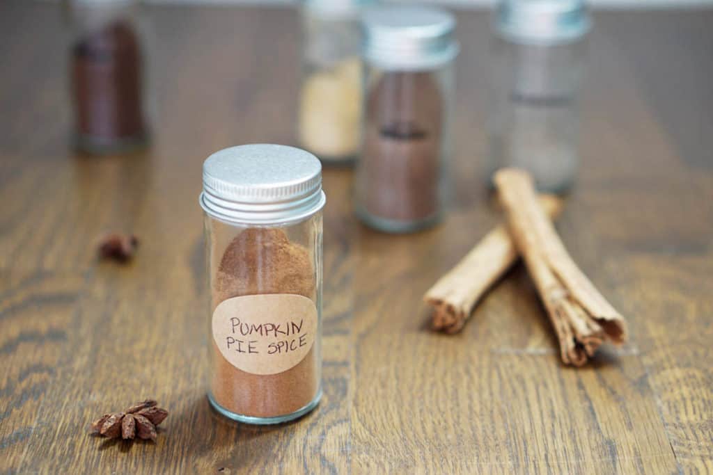  Glass jar of pumpkin pie spice mix on wooden table with other spices around