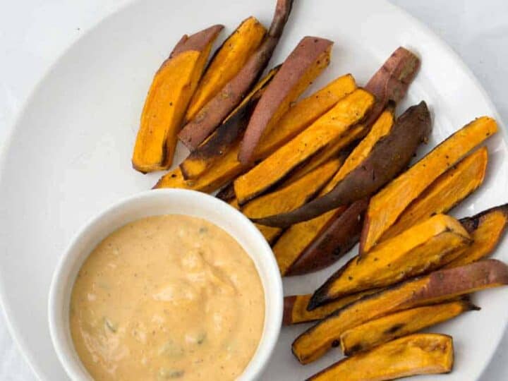 sweet potato fries in fan shape on white plate with white ramekin of spicy dairy free cashew cream sauce
