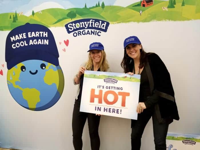 two girls wearing black with a sign saying it's getting hot in here and blue baseball caps saying make earth cool again