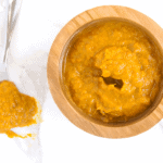 orange Ginger Turmeric Honey Chili Sauce with Dried Red Chilies is spicy, tangy and fresh, making a great marinade, dip, and homemade hot sauce. It's also chocked full of superfoods. in wooden bowl next to spoon dripping sauce on white marble