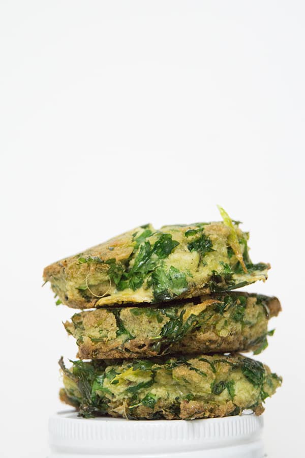 3 celery and parsley fritters stacked on top of each other on white background