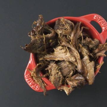 Slow cooked pulled beef in red Staub ramekin on black background