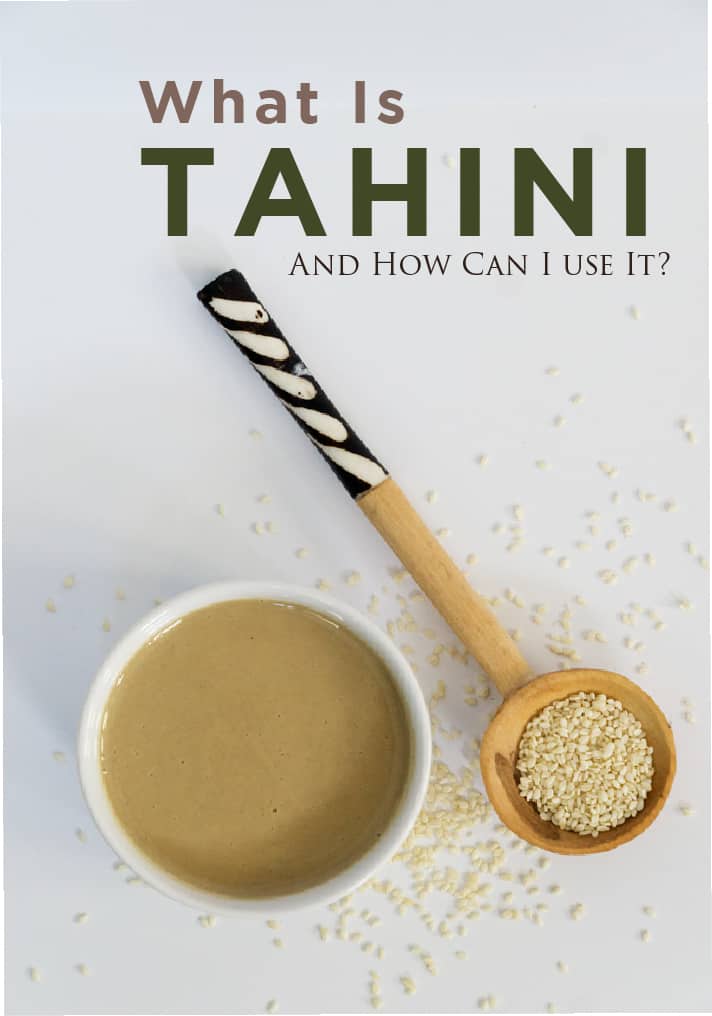 What is Tahini? Is it Dairy Free? And how can I use Tahini in my cooking? Tahini and sesame seeds with wooden spoon on white background.