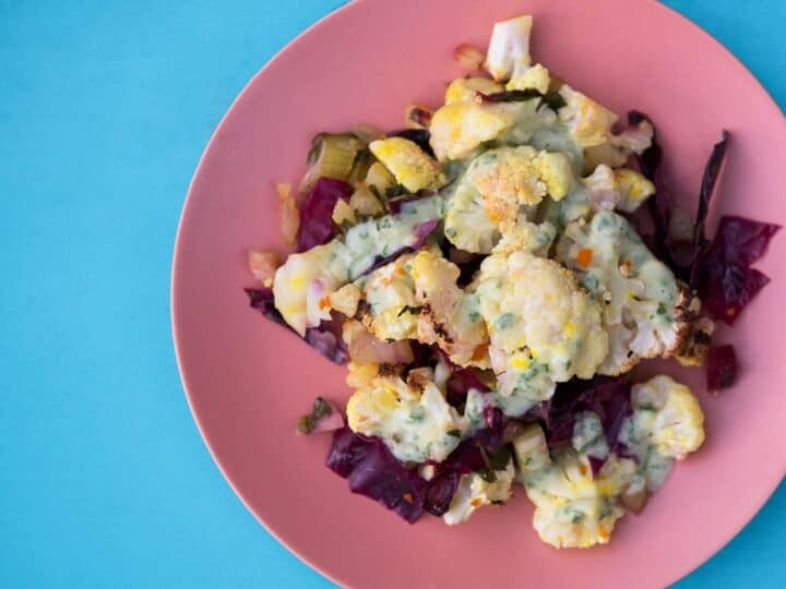 turmeric roasted cauliflower bake on bright pink plate on blue background