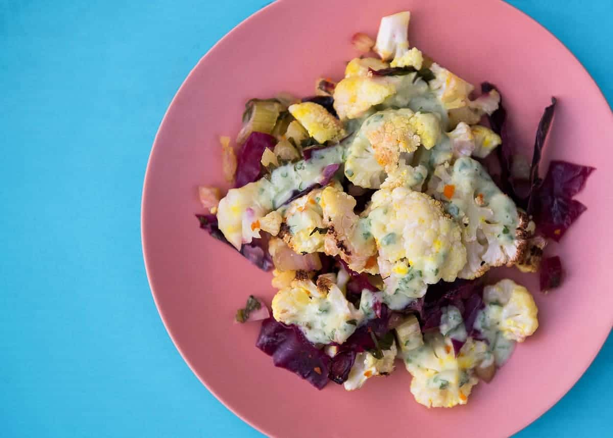 turmeric roasted cauliflower bake on bright pink plate on blue background