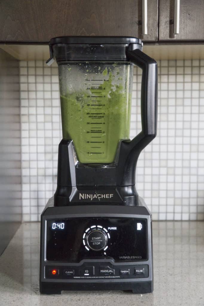 green sauce in blender against white mosaic tile background