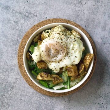 White bowl on cork circle on cement with sauteed cabbage and turnip greens with harissa roasted turnips and broth poached eggs