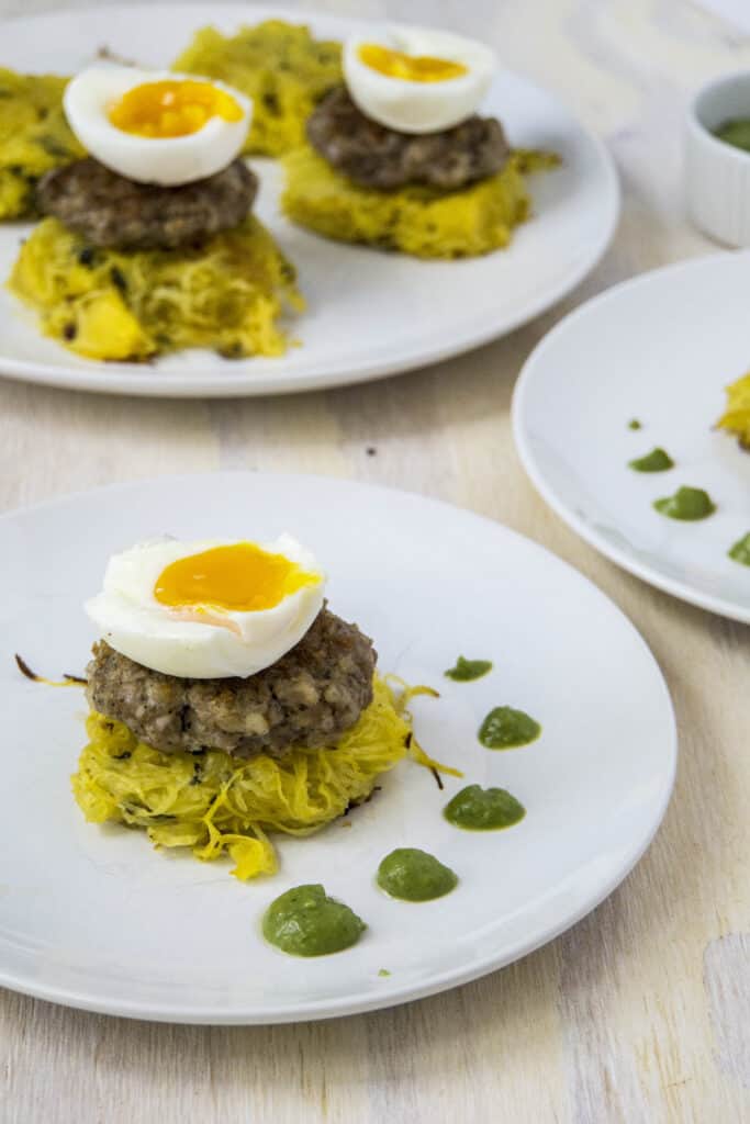 several plates of eggs benedicts, each with 1/2 soft boiled egg over sausage pattie and spaghetti squash next with dotted green sauce