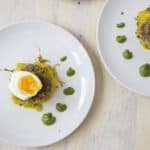1/2 soft boiled egg over sausage pattie and spaghetti squash next with dotted green sauce on white plates