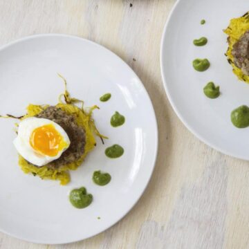 1/2 soft boiled egg over sausage pattie and spaghetti squash next with dotted green sauce on white plates