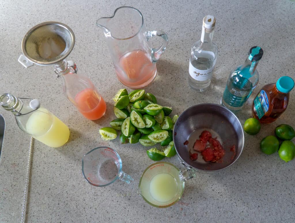 Jars of liquor, batched margaritas and spent limes making batched margaritas