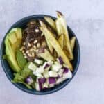 Overhead view of A hand grabs a Fig Tahini Burger bowl with sweet potato fries, kohlrabi and avocado
