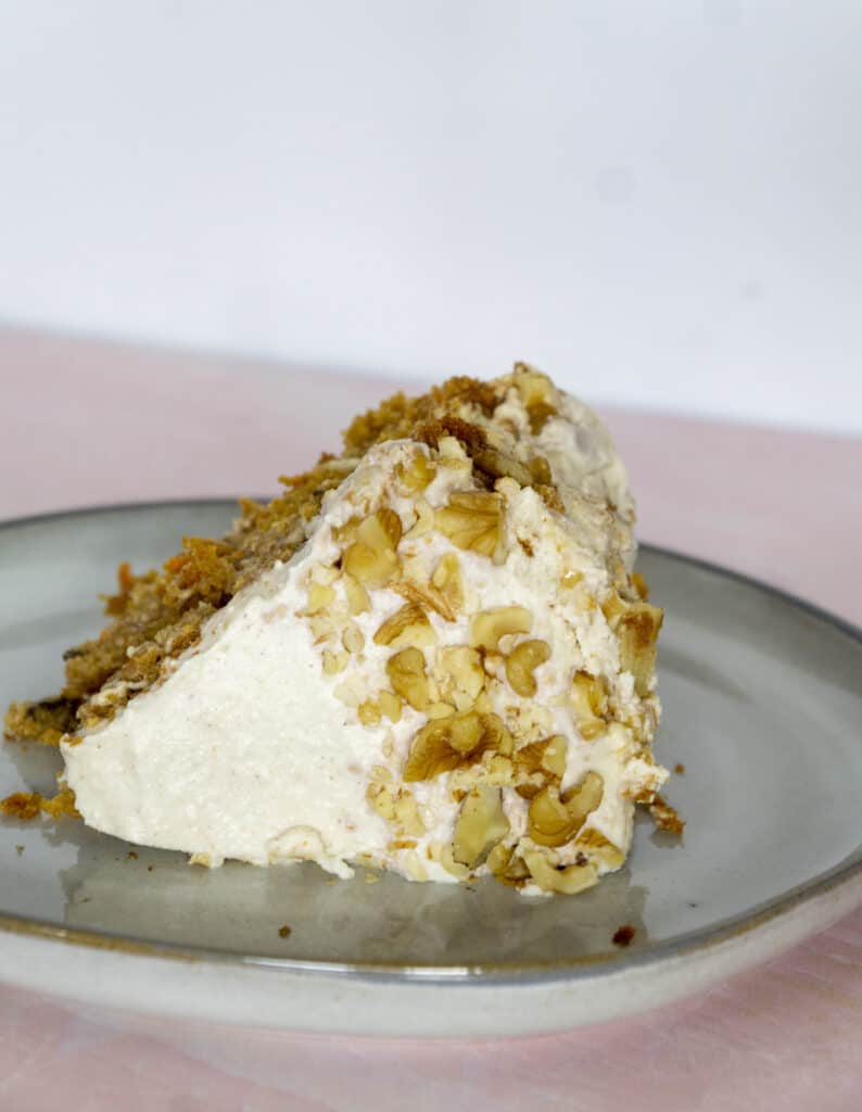 Carrot cake dressed in crushed walnuts sitting on it's side on a pink table