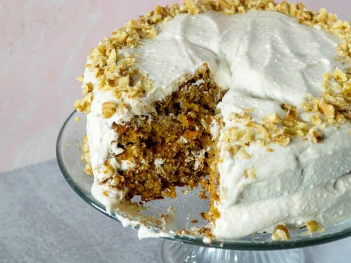 Carrot cake with slice missing and walnut trim on cake plate